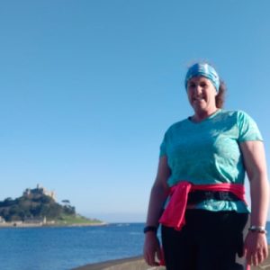 Female in fitness clothing stood with St Michaels Mount and the sea in the distance behind her.