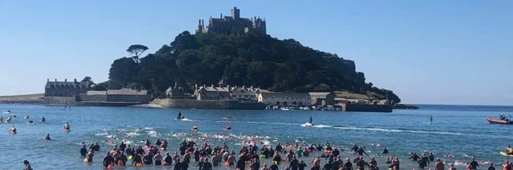 Wide angle image of a large group of swimmers entering the sea in front of St Michaels Mount.